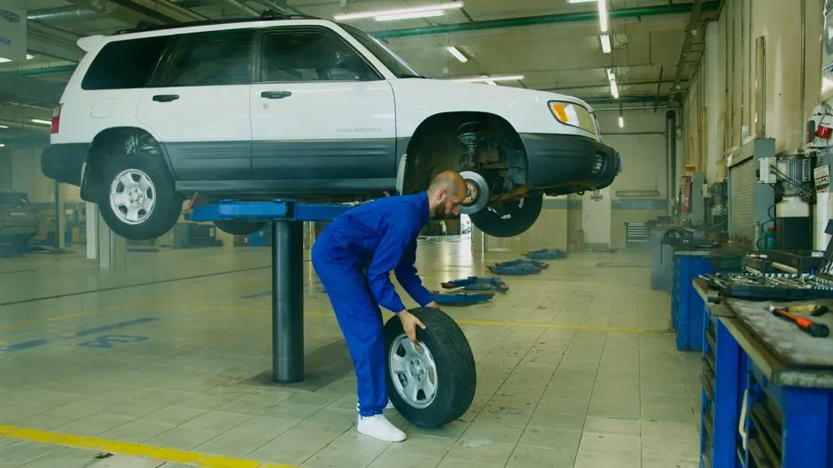 Mechanic holding a tyre beside a car raised on a workshop lift